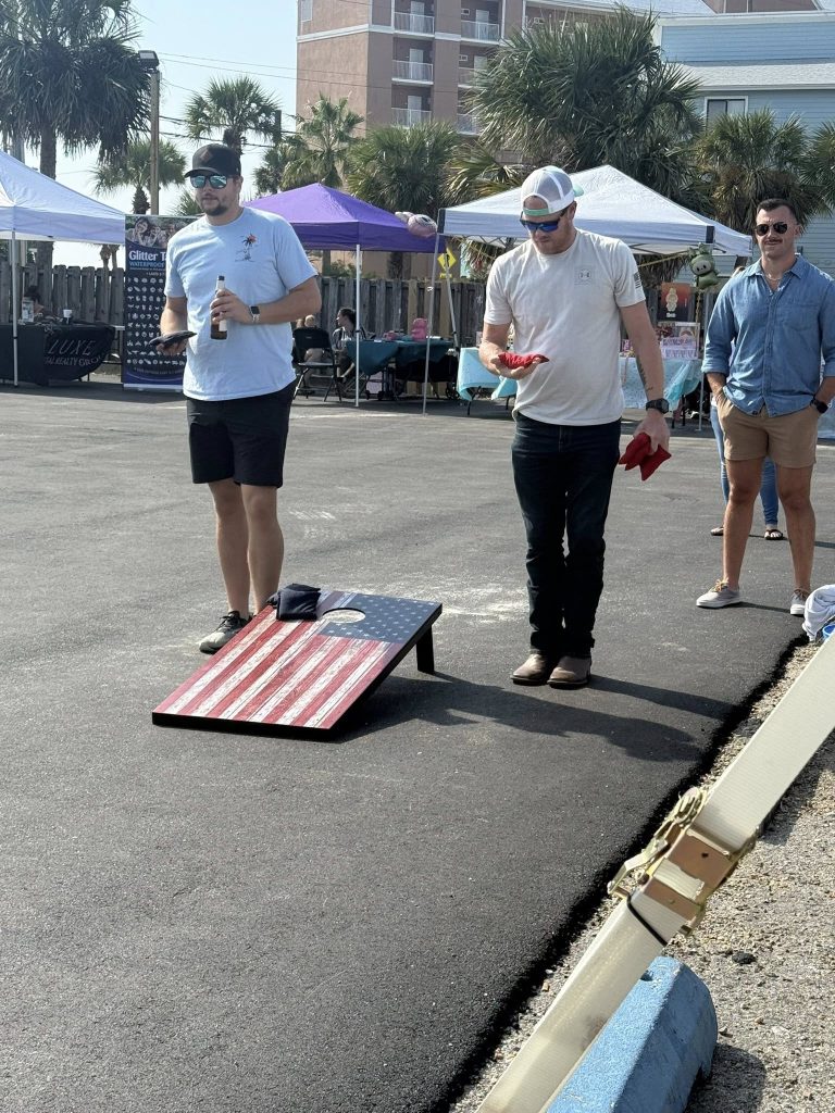Friends playing cornhole outdoors under pop-up tents on a sunny day